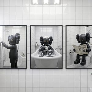 May include: A set of three framed wall art prints featuring a black KAWS character in a white tiled bathroom. The first shows the character reaching for a towel, the second bathing in a tub, and the third sitting on a toilet reading a newspaper.