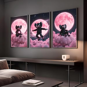 May include: Three framed art prints showcasing a black figure with 'X' eyes set against a pink moon and cloud background. The figure is depicted in various poses, including sitting and floating. The artwork has a contemporary, urban style.