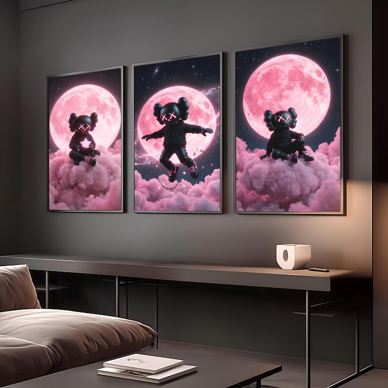 May include: Three framed art prints showcasing a black figure with 'X' eyes set against a pink moon and cloud background. The figure is depicted in various poses, including sitting and floating. The artwork has a contemporary, urban style.