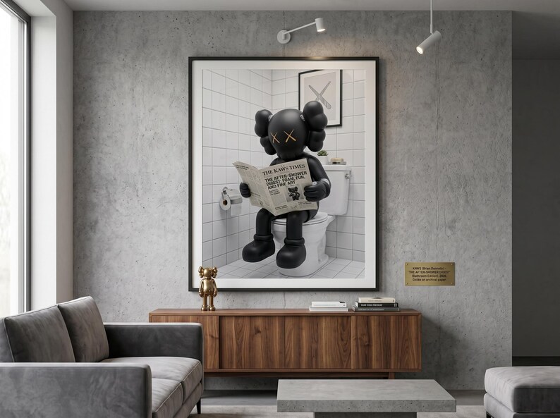 May include: A framed wall art print featuring a black KAWS character sitting on a white toilet while reading a newspaper titled The KAWS Times. The character has signature X-shaped eyes and rounded ears, set against a white tiled bathroom background.