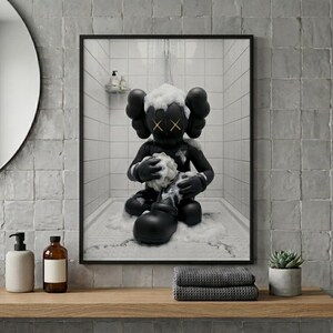 May include: A framed wall art print featuring a black cartoon character with X-shaped eyes sitting in a white tiled shower. The character is covered in white soap suds and is holding a sponge while water falls from a shower head above in the scene.