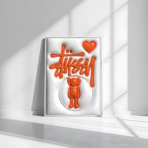 May include: Orange artwork featuring the Stussy logo, a heart, and a KAWS-style figure. The design is raised against a white background, framed in a white border. The artwork is displayed on a white surface with shadows.