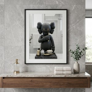 May include: A framed wall art print featuring a black cartoon character with X-shaped eyes, standing on a dark tray with small bottles and a bowl. The character has rounded ears and is positioned in a bathroom setting with a white towel and mirror.