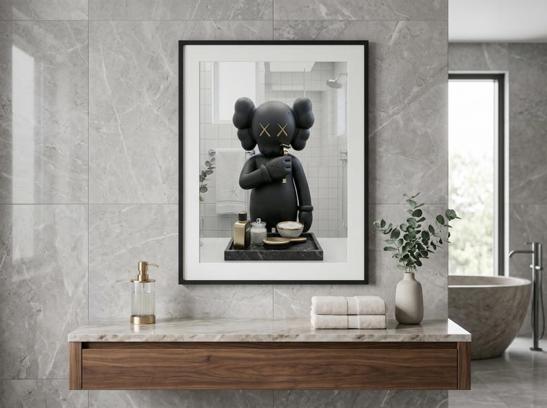 May include: A framed wall art print featuring a black cartoon character with X-shaped eyes, standing on a dark tray with small bottles and a bowl. The character has rounded ears and is positioned in a bathroom setting with a white towel and mirror.