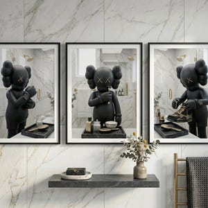 May include: A set of three framed wall art prints featuring a black KAWS character in a bathroom setting. The left print shows the figure adjusting a watch, the centre shows it grooming, and the right shows it holding a sneaker, all in black frames.