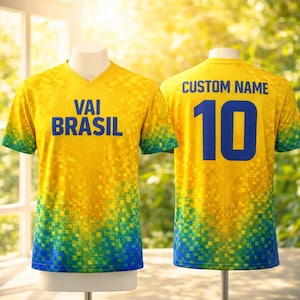 Puede incluir: Una camiseta de f&uacute;tbol amarilla con un dise&ntilde;o pixelado. La parte delantera muestra el texto "VAI BRASIL" en azul. La parte trasera muestra "CUSTOM NAME" encima del n&uacute;mero "10" en azul. La camiseta tiene cuello en V y un degradado verde y azul en las mangas y el dobladillo.