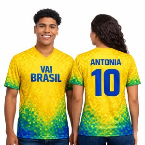 Puede incluir: Camisetas amarillas con cuello en V con un dise&ntilde;o pixelado en amarillo, verde y azul. Una camiseta tiene "VAI BRASIL" en azul, la otra "ANTONIA" y el n&uacute;mero "10" en azul.