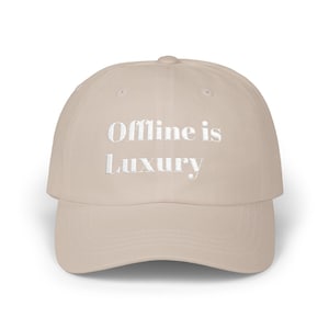 Op de afbeelding: Beige baseballpet met de geborduurde tekst "Offline is Luxury" in het wit. De pet heeft een gebogen klep en een gestructureerde kroon, geschikt voor casual wear.