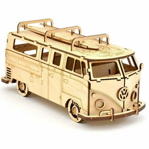 Puede incluir: Maqueta de madera de una furgoneta clásica, con un porta tablas de surf en el techo. La furgoneta tiene cortes detallados para ventanas y puertas, y el icónico logotipo de VW es visible en la parte delantera. El modelo es de madera clara.