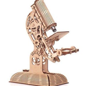 May include: A wooden model of a microscope, featuring intricate gear and lever details. The model is constructed from light-colored wood, with a base, stage, and eyepiece. The design showcases a classic scientific instrument.