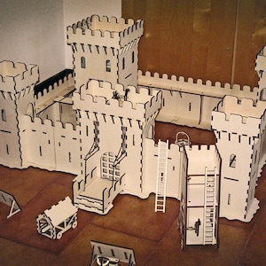Puede incluir: Un gran modelo de castillo de madera sin pintar con varias torres, muros y una puerta. Los componentes de madera adicionales incluyen una catapulta, un carro y una escalera. El modelo está diseñado para el montaje y la exhibición.