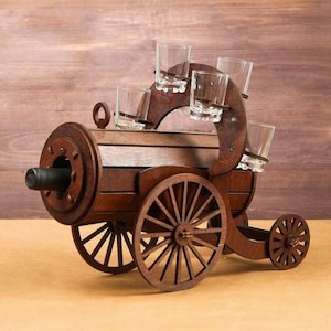 May include: A wooden shot glass and wine bottle holder in the shape of a wagon. The brown holder has five shot glasses and a space for a wine bottle. The wagon has two large wheels and a small wheel.