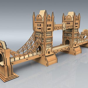Könnte beinhalten: Ein Holzmodell der Tower Bridge mit aufwendigen Ausschnitten. Das Modell besteht aus hellbraunem Holz und umfasst die Türme, Gehwege und Hängekabel der Brücke. Es ist eine detaillierte Nachbildung des berühmten Londoner Wahrzeichens.