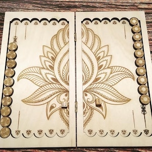 May include: A wooden backgammon board featuring a gold floral design. The open board displays the playing surface, complete with gold game pieces and dice. The rectangular board has a decorative border.