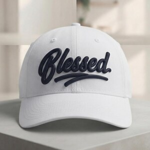 May include: A white baseball cap featuring the word Blessed embroidered in dark navy blue script font across the front panel. The cap has a structured crown, a curved brim, and small ventilation eyelets on the top panels of the fabric.