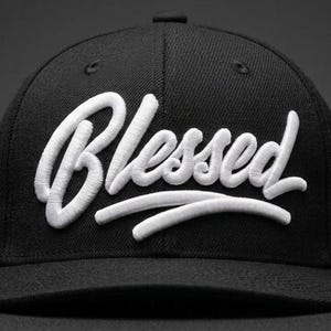 Op de afbeelding: Zwarte baseballcap met het woord "Blessed" in wit geborduurd script over de voorkant. De pet heeft een gebogen klep en een gestructureerde pasvorm, geschikt voor casual wear.