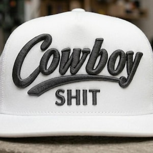 Op de afbeelding: Witte truckerpet met de woorden "Cowboy SHIT" in zwart geborduurd. De pet heeft een gebogen klep en een mesh achterkant. Een casual accessoire voor dagelijks gebruik.