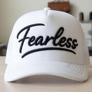 May include: White trucker cap with the word "Fearless" embroidered in black script. The cap has a mesh back and a curved peak. A casual accessory for everyday wear.