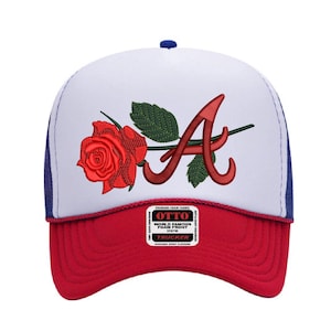 Puede incluir: Gorra de camionero roja, blanca y azul con una rosa roja y la letra "A" bordada en la parte delantera. La gorra tiene una parte delantera de espuma blanca, una visera roja y una parte trasera de malla azul. La etiqueta dice "OTTO".