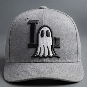 May include: A heather gray baseball cap featuring an embroidered design on the front. The design consists of a large black letter L and a smaller black letter G, with a white ghost figure with black eyes and a black outline positioned in the center.