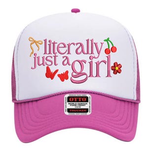 Pode incluir: Boné de caminhoneiro branco e rosa com o texto bordado "literally just a girl" em rosa. O boné apresenta uma aba rosa e costas em malha, com borboletas, cerejas e uma flor bordadas.