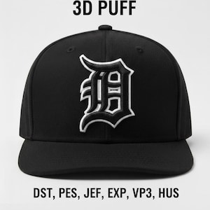 Puede incluir: Gorra de béisbol negra con una letra "D" bordada en blanco y negro. El texto "3D PUFF" está encima de la gorra, y "DST, PES, JEF, EXP, VP3, HUS" debajo. La gorra tiene una visera plana.