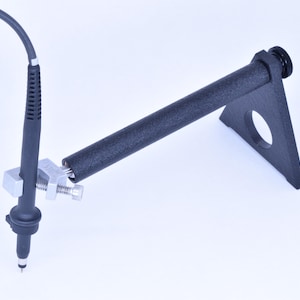 May include: A black probe with a silver clamp is held by a black support arm. The arm is connected to a black triangular base with a circular opening. A black cable extends from the probe.