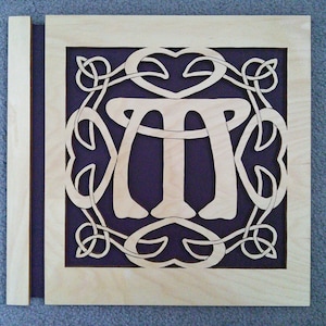 May include: A wooden plaque featuring a Celtic knot design with the letter "M" at its centre. The plaque is painted purple and has a light wood frame.