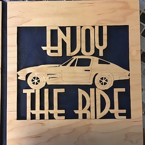 May include: Wooden sign with a blue background and the text "ENJOY THE RIDE" in a vintage font. A silhouette of a classic car is in the centre of the sign.