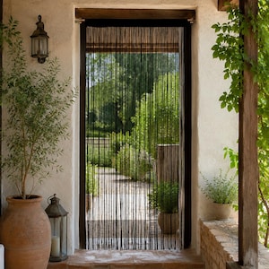 May include: A black string curtain hangs within a doorway, featuring numerous thin, vertical strands that create a semi-transparent barrier. The curtain is mounted on a dark horizontal rod at the top of the frame, allowing light to pass through.
