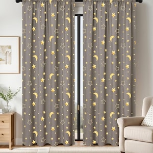 May include: A pair of gray blackout curtains with a repeating pattern of gold stars and crescent moons. The curtains are hanging in front of a window, and are made of a thick, opaque fabric.