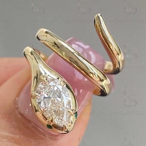 以下が含まれることがあります： 金色の蛇の指輪。蛇の頭には洋梨型の透明な宝石が使われています。指に巻き付くようにデザインされており、尾はカーブしています。蛇の頭には小さな緑色の宝石がアクセントとしてあしらわれています。
