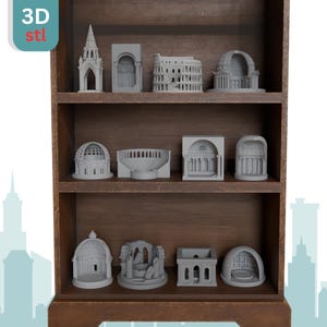 Pode incluir: Uma prateleira de madeira castanha exibe modelos arquitetónicos cinzentos em miniatura, incluindo uma catedral, o Coliseu e outras estruturas clássicas. O texto "3D st" está no canto superior esquerdo. Os modelos estão dispostos em três níveis.