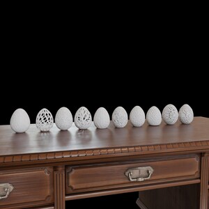 May include: A collection of nine white decorative eggs with various carved designs, displayed on a dark wooden table. The eggs have different patterns, including openwork and textured surfaces, against a black background.