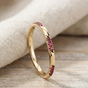 Puede incluir: Un anillo de oro con una fila de pequeñas gemas rojas brillantes. El anillo tiene un acabado liso y pulido y un diseño ligeramente curvado. Las gemas están espaciadas uniformemente y añaden un toque de color.