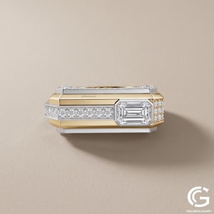 Top-down view of a rectangular two-tone statement ring. The flat upper surface displays a straight channel of pave diamonds leading to a prominent, bezel-set emerald-cut diamond positioned near the right edge.