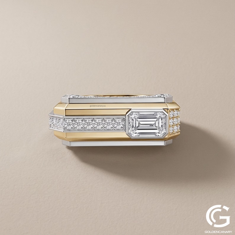 Top-down view of a rectangular two-tone statement ring. The flat upper surface displays a straight channel of pave diamonds leading to a prominent, bezel-set emerald-cut diamond positioned near the right edge.