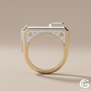 Side profile view of an architectural, two-tone gold ring standing upright. The flat-top design showcases a white gold side plate encrusted with pave diamonds and secured by two yellow gold screws, with a raised emerald-cut diamond visible on top.