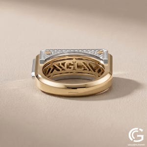 Low-angle view focusing on the under-gallery of a chunky gold men's ring. The interior of the band reveals an intricate, cut-out geometric lattice design beneath the main setting, contrasting with the smooth, polished yellow gold of the lower band.