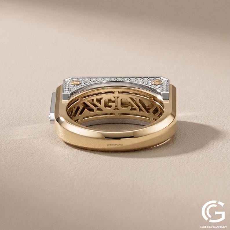 Low-angle view focusing on the under-gallery of a chunky gold men's ring. The interior of the band reveals an intricate, cut-out geometric lattice design beneath the main setting, contrasting with the smooth, polished yellow gold of the lower band.