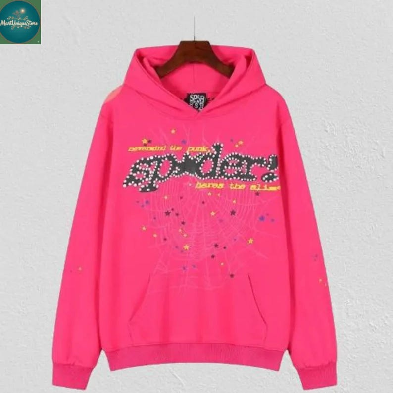 May include: A bright pink hoodie with a front pocket and a hood. The hoodie features the word "sp5der" in a stylized font, along with a spiderweb design and text that reads "defended the punk" and "bares the alibi".