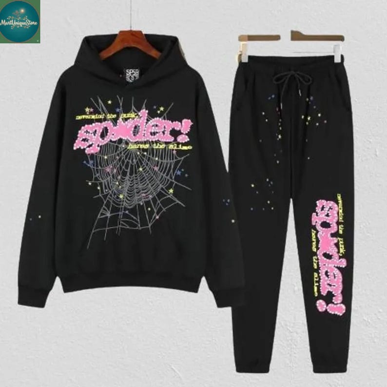 May include: Black hoodie and sweatpants set. The hoodie features a pink "Spider!" graphic with a spiderweb design. The sweatpants have a matching pink graphic on the leg and a drawstring waist. The set is made of a soft material.