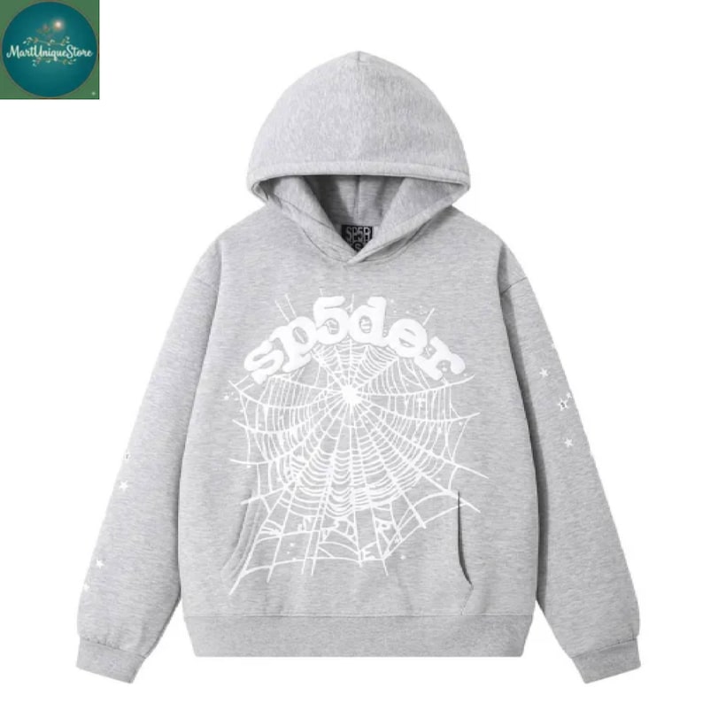 Puede incluir: Sudadera con capucha gris con un dise&ntilde;o de telara&ntilde;a blanca y la palabra "sp5der" en el pecho. La sudadera tiene un bolsillo delantero y estrellas en las mangas.