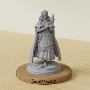 Op de afbeelding: Een grijze hars miniatuurfiguur van een staand personage met een lange mantel, een gedetailleerd lijfje en een gelaagde rok. Het figuur houdt een vlam in één hand en staat op een ronde basis met een boek, met de tekst Soul Sculpt op de voet.