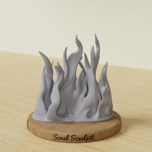 Puede incluir: Escultura gris de llamas estilizadas sobre una base redonda de madera. La escultura tiene un acabado liso y lleva la inscripción "Soul Sculpt" en letra cursiva.