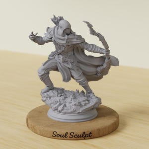 May include: A gray figurine of an archer in a hooded cloak, drawing a bow. The figure is posed on a rocky base, mounted on a wooden disc. The text "Soul Sculpt" is printed on the wooden base.