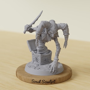 Puede incluir: Una escultura gris de una figura de bufón amenazante que emerge de un cofre del tesoro, sosteniendo una cuchilla curva. La figura tiene un cuerpo retorcido y alargado y una sonrisa siniestra. La escultura está montada sobre una base de madera con el texto "Soul Sculpt".