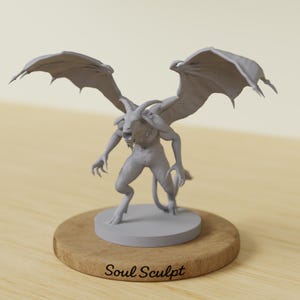 Può includere: Scultura grigia di una creatura demoniaca con grandi ali, corna e artigli. La figura è su una base circolare, posta su una superficie di legno. Il testo "Soul Sculpt" è nella parte inferiore della base di legno.