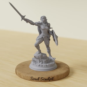 Könnte beinhalten: Graue Figur einer Kriegerin, die ein Schwert und einen Schild hält. Die Figur steht auf einem felsigen Sockel, der auf einer Holzscheibe montiert ist. Der Text "Soul Sculpt" ist auf der Holzbasis aufgedruckt.