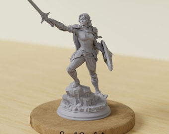 May include: A gray figurine of a warrior woman holding a sword aloft and a shield. The figure is standing on a rocky base, mounted on a wooden disc. The text "Soul Sculpt" is printed on the wooden base.